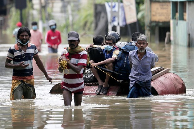 A man pulls a boat made of barrels, to move people from a flooded residential area in Colombo