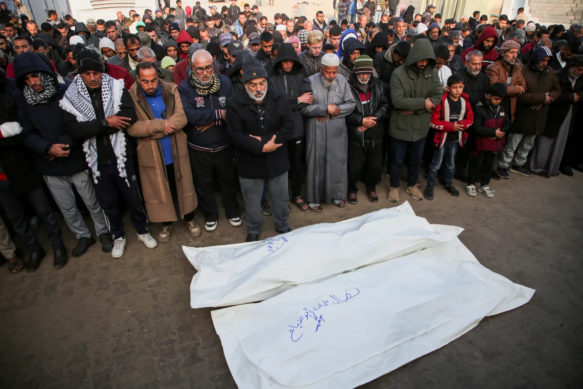 Mourners pray beside the bodies of Palestinians killed in Israeli air strikes, at Nasser Hospital. [Hatem Khaled/Reuters]