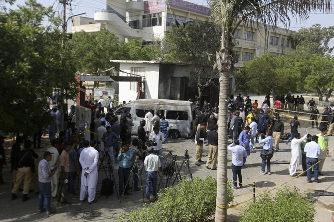 Pakistani police officers and journalists gather near a burned van at the site of an explosion, in Karachi, Pakistan.