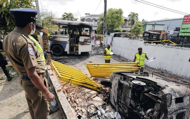 Officers inspect damaged vehicles after they were set on fire by demonstrators at the top of the road to Sri Lankan President's residence during a protest against him.