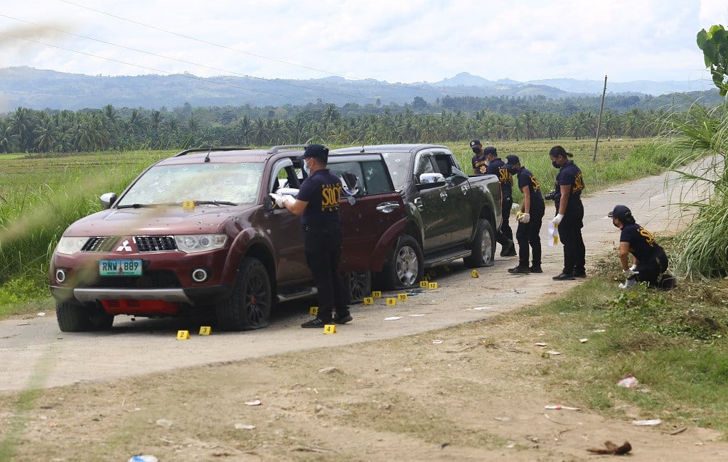 Philippine police investigators look for evidence next to bullet-riddled vehicles after a convoy of SUVs was ambush along a farm-lined road in Guindulungan town