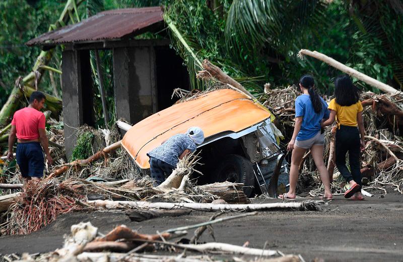 Residents examine a buried passenger jeepney swept away retrieve by floods during heavy rains brought about by Tropical Storm Trami.