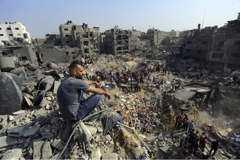 A man sits on the rubble as others wander among debris of buildings that were targeted by Israeli airstrikes in Jabaliya refugee camp, northern Gaza Strip. Photo: Abed Khaled/ The AP