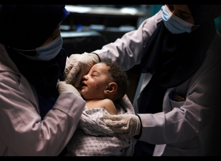 A nurse holds a baby who was pulled alive from under the rubble after the Israeli air raid [Mahmud Hams/AFP]