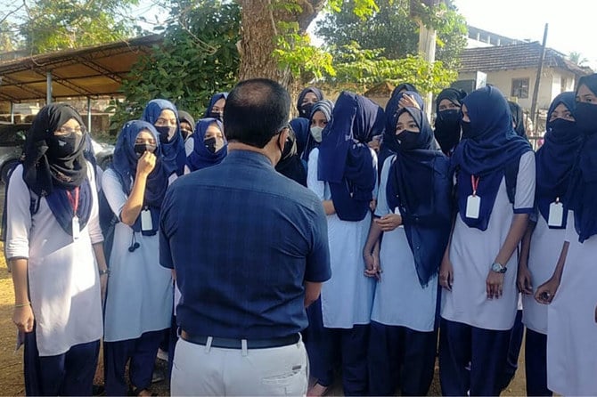 Indian girl students who were barred from entering their classrooms for wearing hijab speak to their principal outside the college campus in Udupi, India.